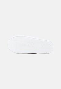 Zapatilla blanca sin cordones con un patrón texturado en la parte superior y una suela de goma texturada, con un borde redondeado y marcaje de talla.