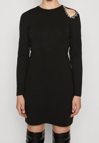 Svart långärmad klänning med en axelöppning prydd med pärldetaljer, som har en figurnära silhuett och slät textur.