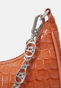 Gros plan sur le coin d’un sac à main orange à texture crocodile avec une chaîne argentée et un fermoir.