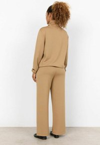 Beige, zachte gebreide turtleneck sweatshirt met losse mouwen, gecombineerd met bijpassende wijde broek. Gladde textuur, relaxte pasvorm, minimale details.