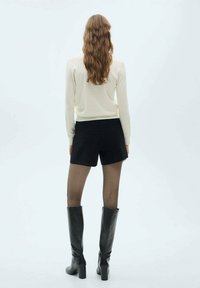 Maglione in maglia di crema, pantaloni neri corti e stivali alti in pelle nera. Capelli lunghi e mossi, collant trasparenti. Design semplice con attenzione al fit e alla texture.