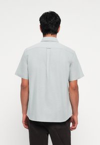 Short-sleeve shirt in light grey fabric with a spread collar, back pleat, and a straight hem. Smooth texture, minimal design.
