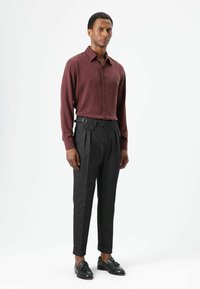 Bordeauxrode blouse met knopen, gecombineerd met hooggetailleerde grijze broek met ceintuur en plooien. Zwarte loafers maken de look compleet.