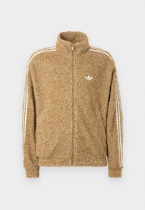 Καφέ, φ fuzzy fleece jacket με ψηλό γιακά, πλήρη φερμουάρ και λευκές λωρίδες στα πλάγια. Διαθέτει ένα μικρό λευκό λογότυπο στο στήθος.