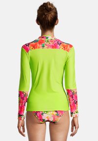 Rash guard à manches longues en vert néon vif avec des accents floraux sur les épaules et les manches, doté d'une coupe ajustée et d'une texture douce et lisse.