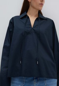 Top a maniche lunghe blu navy con una vestibilità rilassata, caratterizzato da scollatura a V, coulisse regolabile e un tessuto testurizzato.