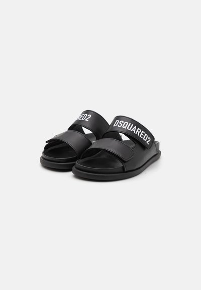 Mustat liukusandaalit leveillä strap-onilla, joissa on valkoinen "DSQUARED2" -teksti. Pehmeä nahkamateriaali, litteä pohja, avonainen kärki.