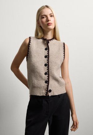 Gilet lavorato a maglia in beige con coste verticali, chiusura con bottoni neri e un bordo scuro a contrasto lungo il colletto e le armature.