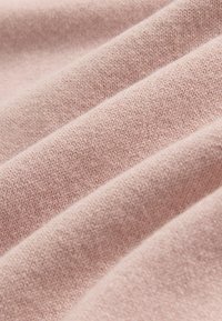 Weicher, hellrosa gestrickter Stoff mit feinen, gleichmäßigen Maschen und sanften Falten, die ein texturiertes, gemütliches Aussehen schaffen.