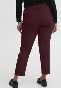 Pantalons bordeaux avec une texture lisse, taille élastique et coupe droite. Portés avec des mocassins noirs, dotés de poches arrière discrètes.
