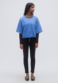 Μπλε cropped φούτερ με κοντά μανίκια, φορεμένο πάνω από μαύρο μακρυμάνικο τοπ, συνδυασμένο με μαύρο στενό τζιν και καφέ μπαλαρίνες.