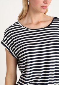 Camiseta de rayas en azul marino y blanco, hecha de una tela suave, con escote redondeado y mangas cortas enrolladas. Sin texturas o patrones notables.