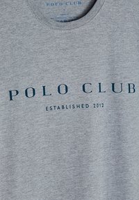 Světlě šedé tričko s kulatým výstřihem a tmavě modrým nápisem "POLO CLUB" a menším textem "ESTABLISHED 2012" na přední straně.