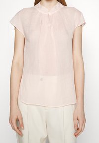 Blusa corta a maniche corte di colore rosa chiaro con colletto alzato, chiusura con un bottone e tessuto morbido e testurizzato. Orlo curvato per una vestibilità rilassata.