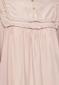 Ljusrosa klänning med volangkrage, subtil randig textur och knappstängning vid bröstet. Flödande design med rynkad midja.
