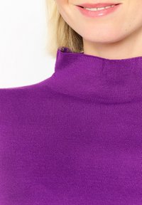 Top de cuello alto morado ajustado, hecho de tela canalé, que presenta un escote alto y una textura suave, enfocándose en un color vibrante.