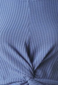 Tamno plavi rebrasti materijal s uvijenim prednjim detaljem. Tekstura je meka, s vertikalnim crtama i glatkim završetkom.