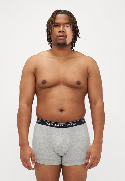 Grau Baumwoll-Boxershorts mit einem schwarzen Bund, auf dem "POLO RALPH LAUREN" steht. Das Modell steht frontal, mit sichtbarem Oberkörper und Armen.