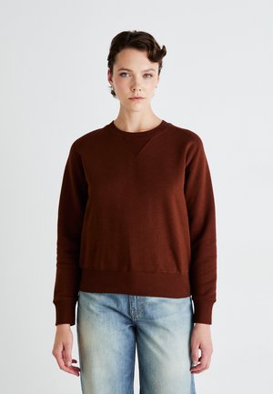 Brun bomulds-sweatshirt med rund hals og ribbede manchetter, som har en afslappet pasform og en subtil tekstur. Matchet med lyseblå denimjeans.