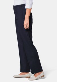 Marineblauwe, hoog-waisted broek met een rechte snit en elastische tailleband, gecombineerd met lichtbeige instappers.