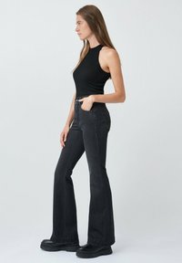 Un débardeur noir à côtes associé à un jean flare en denim foncé taille haute. Le mannequin porte des bottes à plateforme noires. Design simple et épuré sans motifs.
