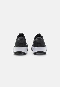 Zapatos deportivos negros con parte superior de malla, suelas blancas y una pestaña en el talón; presentan un patrón texturizado en la parte superior.