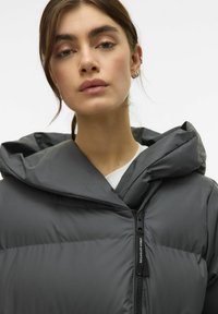 Graue Daunenjacke mit Kapuze, hoher Stehkragen und einem Frontreißverschluss. Glatte Textur mit einem einfachen Urban Adventure-Label in der Nähe des Reißverschlusses.