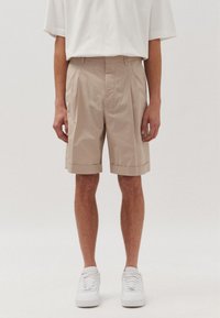 Pantaloni corti beige sartoriali con pieghe, orli risvoltati e tasche laterali. Abbinati a sneakers bianche e una T-shirt bianca dalla vestibilità ampia.