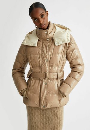 Giacca a vento beige con vita cintata, colletto alto e cappuccio crema a contrasto. Tessuto testurizzato con motivi trapuntati e bottoni metallici.