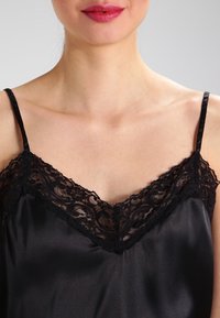 Camisole en satin noir avec bordure en dentelle au niveau de l'encolure, dotée de fines bretelles réglables et d'une texture lisse.