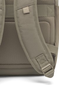 Rucsac gri cu curele din plasă captusită și fabrică texturată. Prezintă o etichetă cu logo și curele reglabile. Construcție robustă cu un anumit luciu.