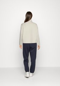 Jasnoszara, bluza z wysokim kołnierzem w połączeniu z granatowymi dresami. Ubranie ma luźny krój i jest wykonane z miękkiego materiału.