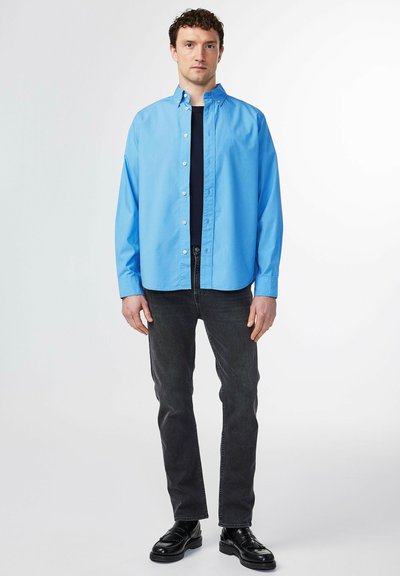 Lichtblauw overhemd met kraag, gecombineerd met donkere jeans en zwarte schoenen; heeft lange mouwen en een relaxte pasvorm.