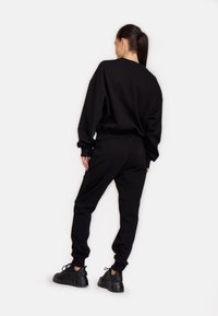 Fekete, oversized kapucnis pulóver és hozzá illő melegítőnadrág, pamutkeverékből, bordás mandzsettákkal, laza szabású és kerek nyakkivágással, vastag fekete sportcipővel párosítva.