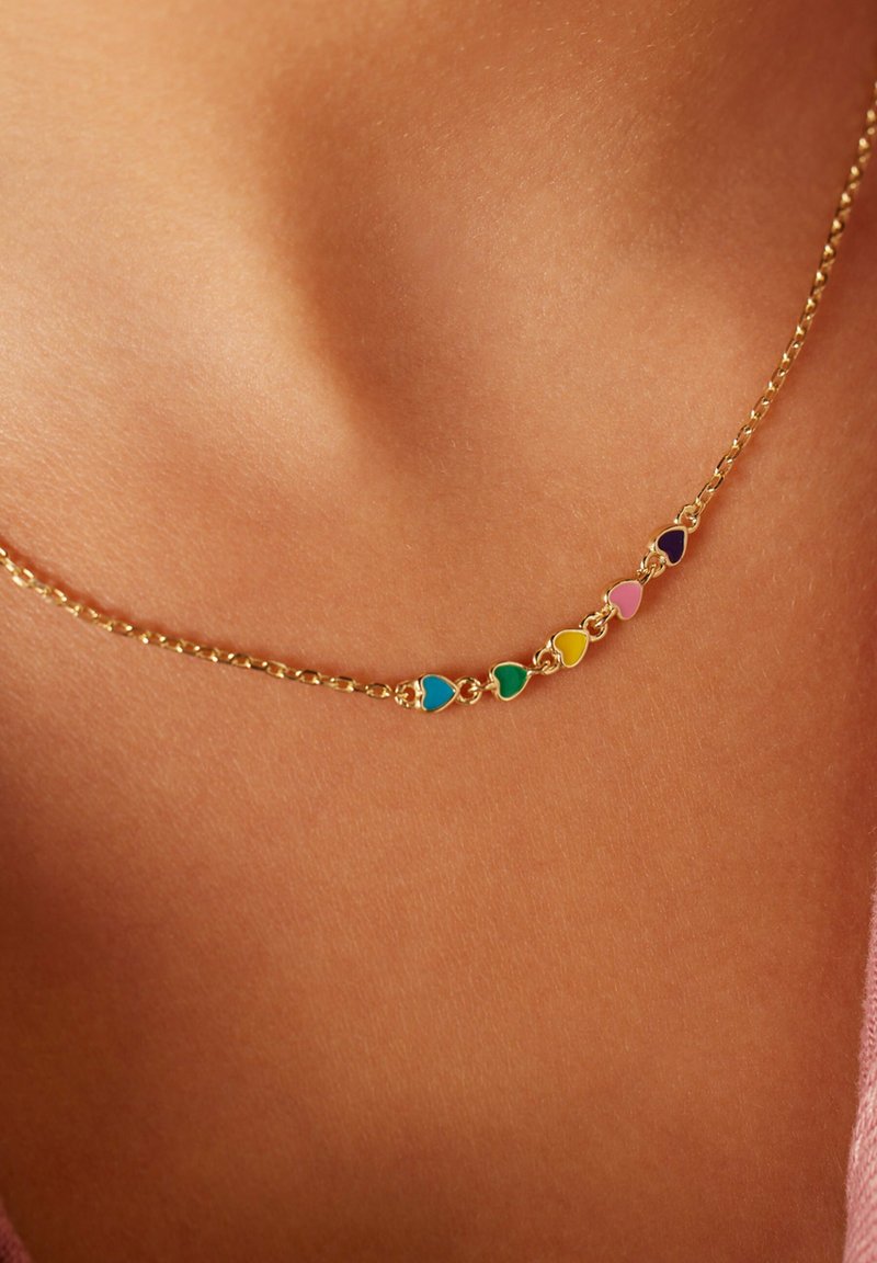 Gouden ketting met afwisselende hartvormige bedels in teal, groen, geel, roze en paars, tegen een huidkleurige achtergrond.