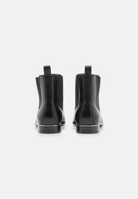 Paire de bottines Chelsea en cuir noir vues de dos, dotées de languettes de tirage et de panneaux latéraux élastiques, sur un fond blanc uni.