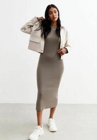 Geribbelde midi-jurk in een gedempt groen, gecombineerd met een cropped beigejack met voorzakken. Draag het met witte sneakers voor een casual uitstraling.