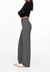 Grijze wijde broek gemaakt van gestructureerde stof, met een hoge tailleband, gecombineerd met witte sneakers. De top is zwart en strak.