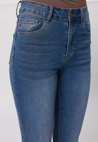 Denimjeans in mittlerem Blauton, im Hochbund-Design, mit klassischem Fünf-Taschen-Stil und subtilen Waschungen auf dem Stoff.