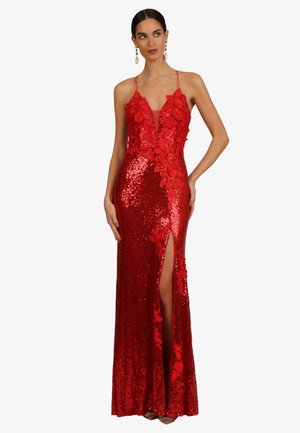 Frau trägt ein bodenlanges rotes Paillettenkleid mit floralen Verzierungen, Spaghettiträgern, tiefem V-Ausschnitt und einem vorderen Oberschenkelschlitz, steht still.