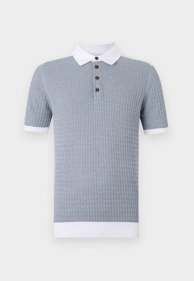 Svetlomodrá polokošeľa s krátkym rukávom a textúrovaným vzorom, bielym golierom a tromi hnedými gombíkmi. Pevné biele manžety na koncoch rukávov.