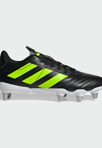 Zwarte voetbalschoenen met neon groene strepen, bovenwerk van textuurleer, witte zool en metallic noppen voor grip op grasoppervlakken.