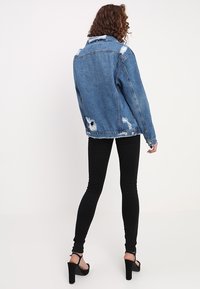 Farkkutakki, jossa on kulutettu yksityiskohtia, sininen väri, rento malli ja rikkinäinen helma, yhdistettynä mustiin skinny-farkkuihin ja korkokenkiin.