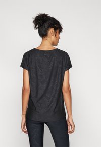 Black short-sleeve t-shirt with a textured snake skin pattern, curved hem, and a relaxed fit. Worn with matching black leggings.