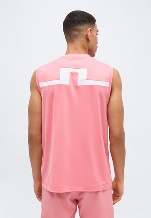 Muž, ktorý má na sebe ružový tielko bez rukávov s bielym geometrickým vzorom na hornej časti chrbta, stojaci chrbtom k nám.