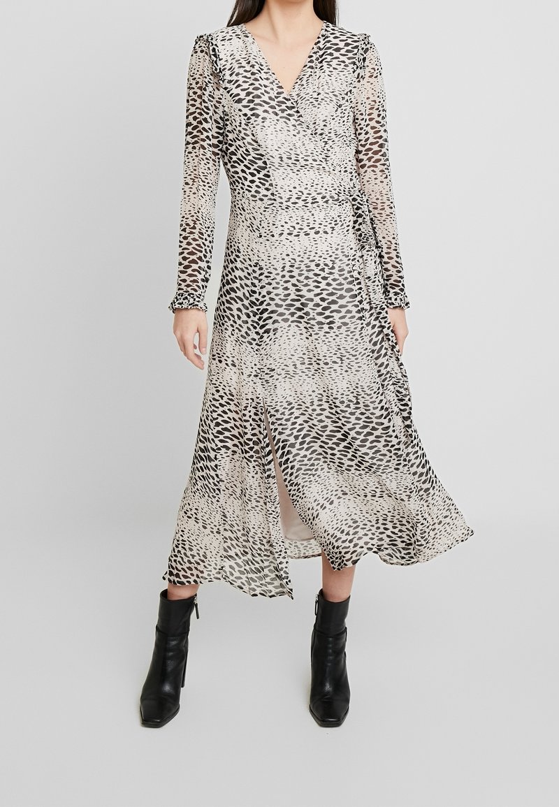 Langärmliges Wickelkleid aus transparenter Stoff mit einem schwarz-beigen Tiermotiv, verziert mit Rüschendetails und einem Schlitz vorne. Getragen mit schwarzen Ankle Boots.
