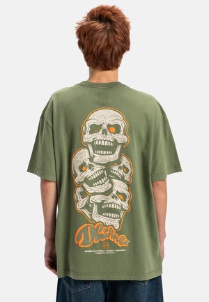 Olijfgroene oversized t-shirt met een grafisch ontwerp van drie schedels in wit en oranje op de achterkant. Zacht katoen, relaxte pasvorm.