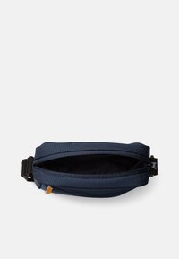 Borsa in tessuto blu navy con apertura con zip, forma rettangolare piatta e superficie texturizzata. Presenta una cintura con fibbia su un lato.