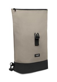 Béžový látkový batoh s čiernym dnom, horným zipsom a čiernym nastaviteľným popruhom s prackou. Obsahuje štítok na prednej strane.