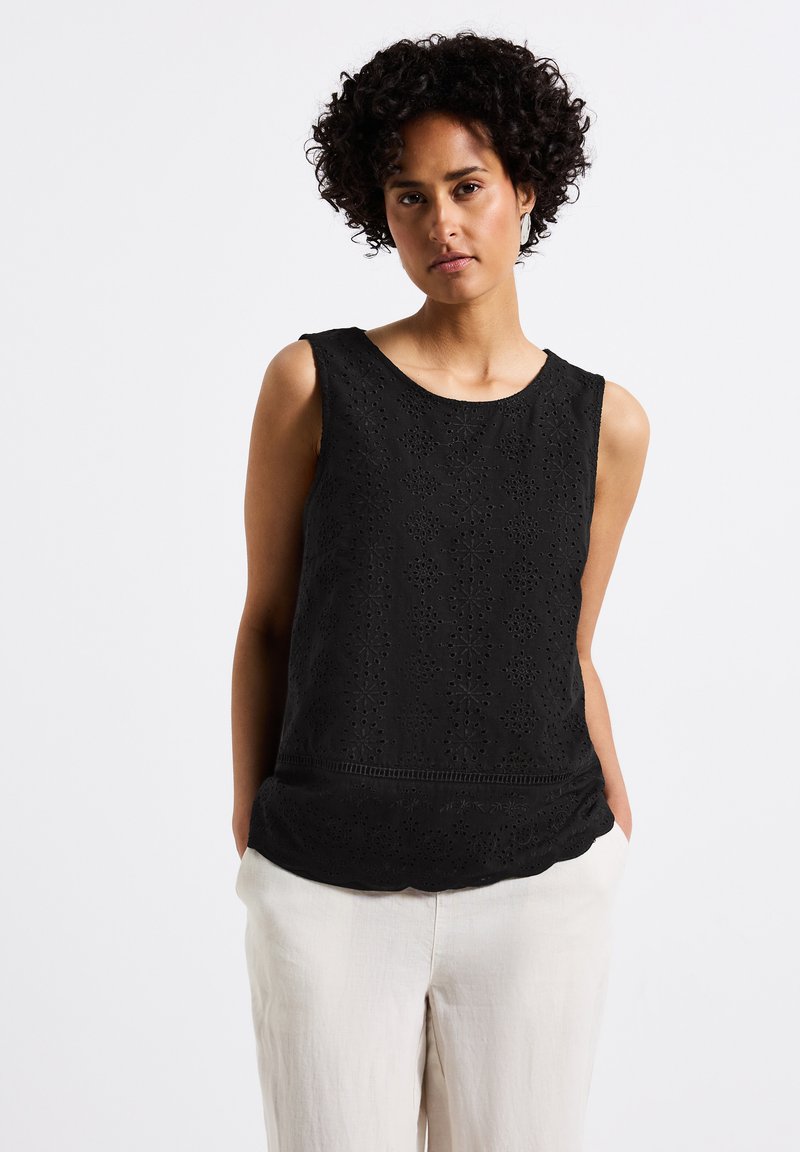 Svart ärmlös topp med texturerad blommig broderi och scallopad fåll. Kombinerad med ljusa lösa byxor som visar en avslappnad passform.